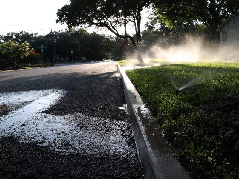 Water flows into the street while sprinklers water a lawn in Alamo Heights Tuesday.