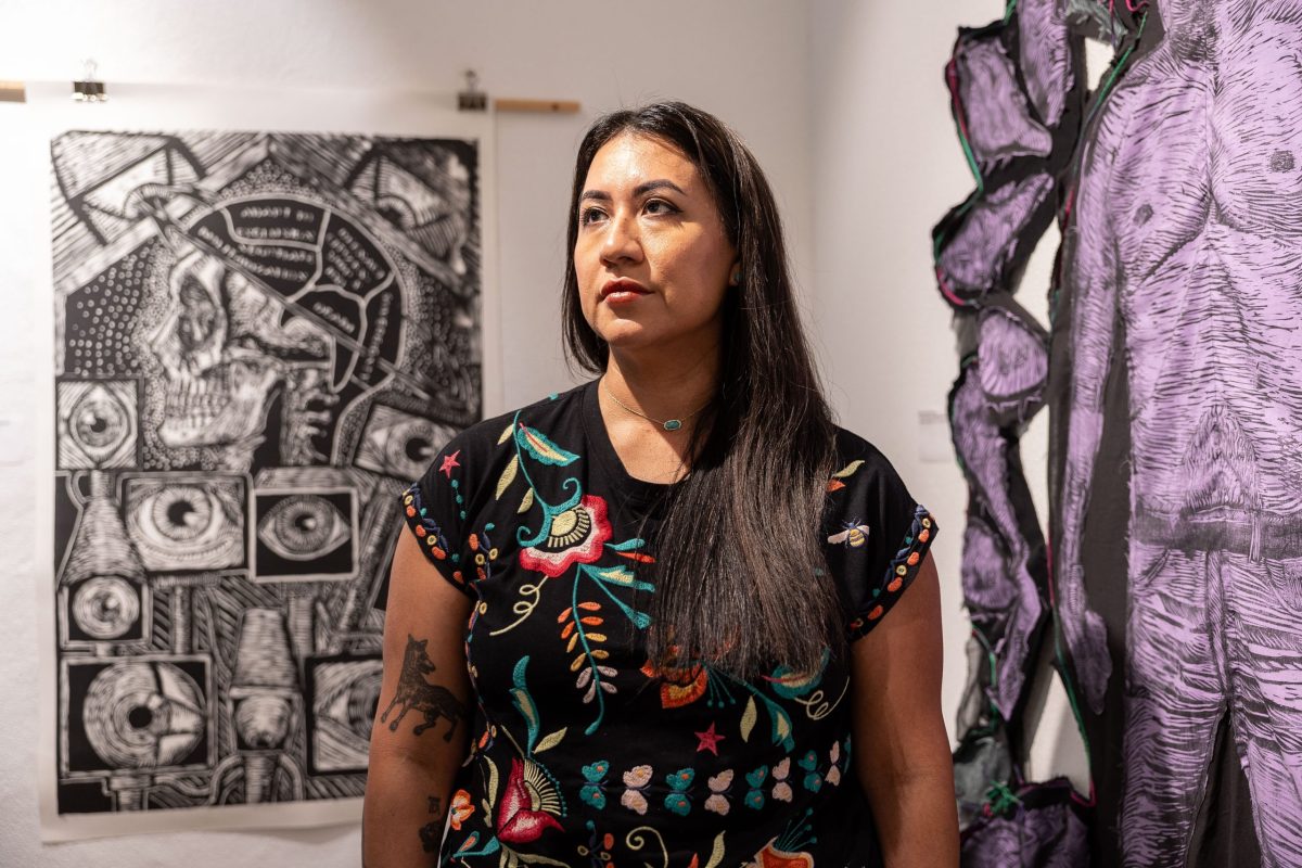 Artist Celeste de Luna poses in front of two of her artworks on display inside of Guadalupe Bookstore as part of the Life and Death on the Border 1910-1920 traveling exhibit created by Refusing to Forget.