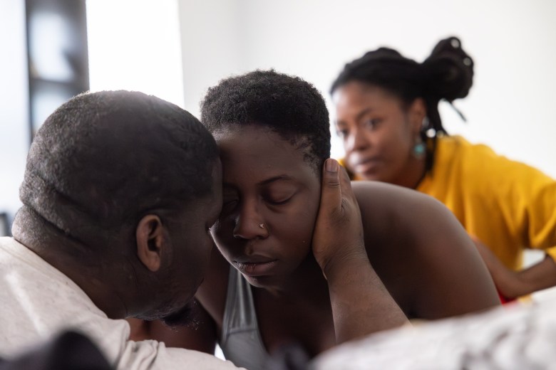 Davonte Head holds his wife Genise Head as she works through strong contractions in their home Tuesday. Head's doula Loreal James does hip massages to help with the pain and help prepare Head for birth in a few hours.