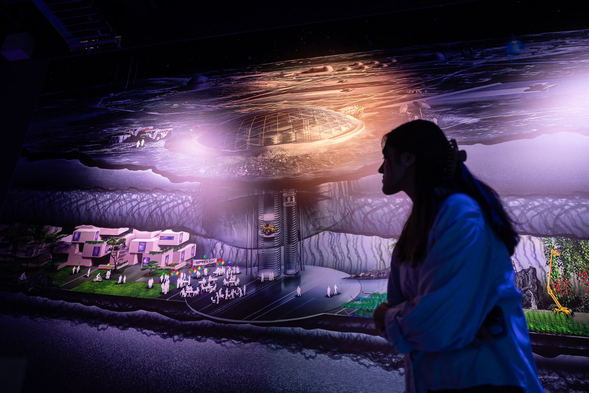 Siddhi Raut, who completed the third cohort of the LCATS program, stands in front of a large rendering on display inside of SAMSAT showing what life could look like inside caves on the moon. Raut worked on a rocket launch and a high altitude balloon when she completed the program in 2017.