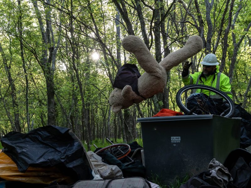 A City Waste Management worker throws away a giant teddy bear left behind by a homeless couple in the encampment they called home for roughly two months in a wooded area off of Thousand Oaks Drive in North San Antonio early Tuesday morning.