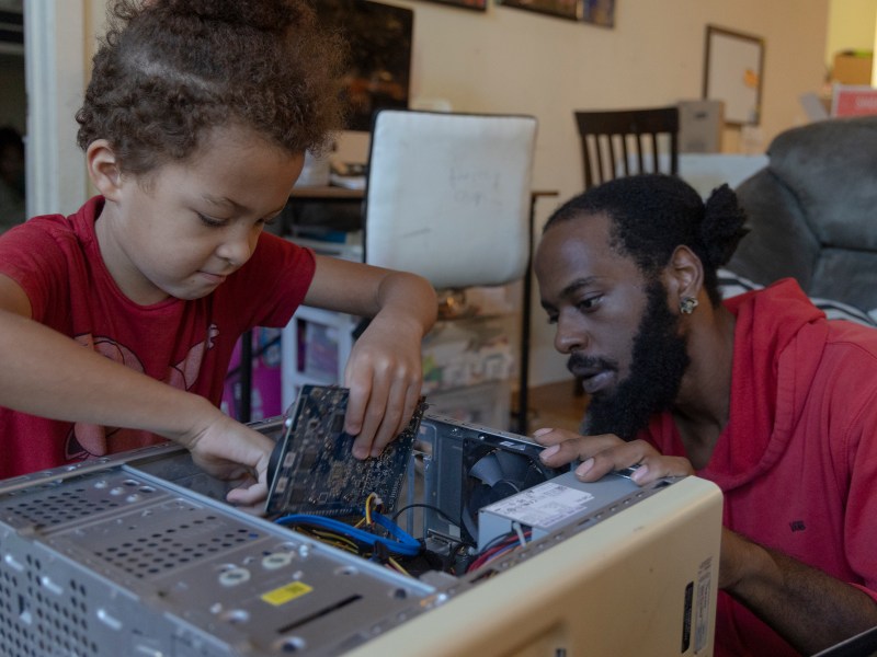 Dyvontrae Johnson watches his son Atticus, 7, install parts into an old computer Wednesday.