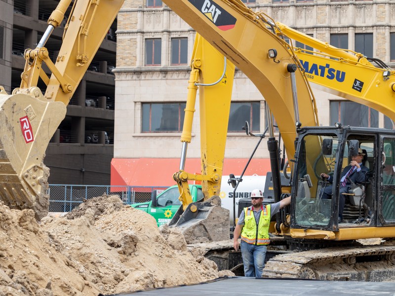 County Judge Nelson Wolff uses an excavator to take the first scoop of dirt during the official groundbreaking for downtown’s first multi-family high-rise.