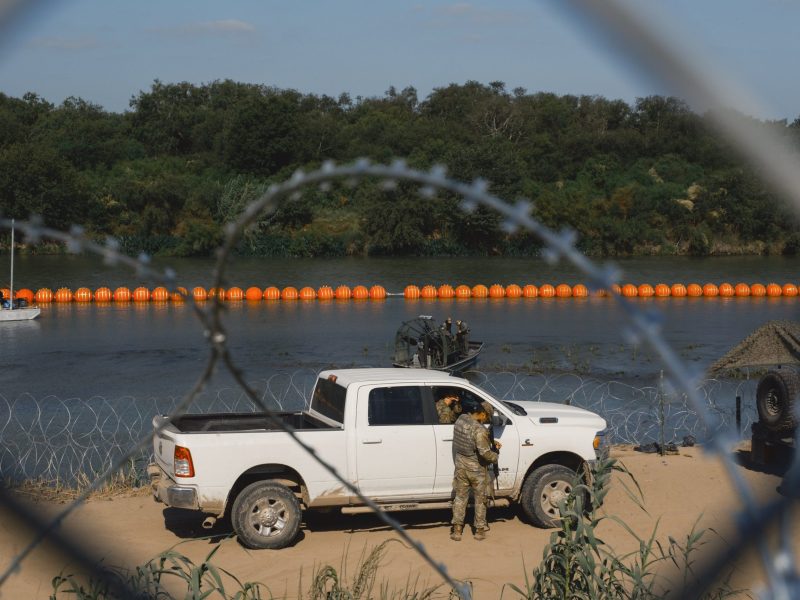 State law enforcement officers stand guard as workers deploy a string of buoys to prevent migrants from swimming across the Rio Grande in Eagle Pass on July 14. A state trooper has alleged that officers deployed as part of Gov. Greg Abbott's Operation Lone Star were ordered to push migrants, including children, back into the river.