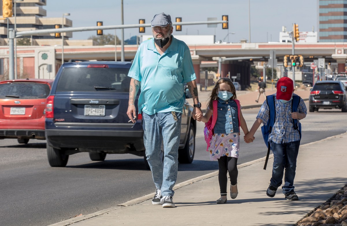 Pedestrians walk along a sidewalk as cars pass by on San Pedro Avenue on Wednesday.