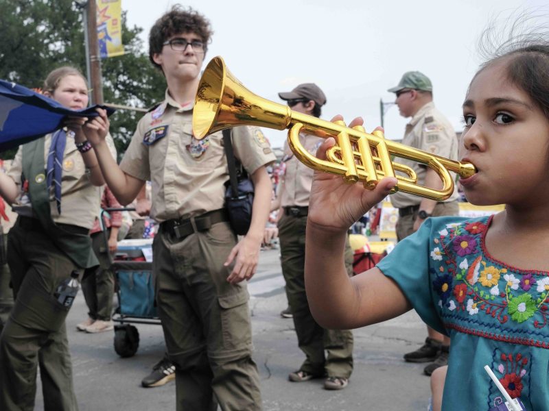 A parade attendee blows a toy trumpet as the Alamo Area Boy Scouts of America march during the 2024 Battle of Flowers Parade.