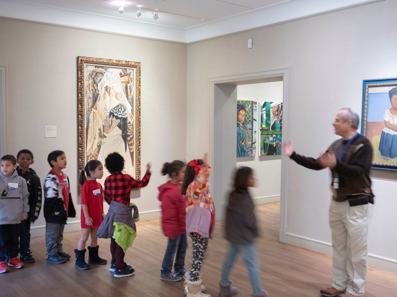 Children in a school group pass by Protectors of Memory: Court of Dreams and Protectors of Memory: Charlene (Reimagined) on view in the Zoch Gallery at the McNay Art Museum.