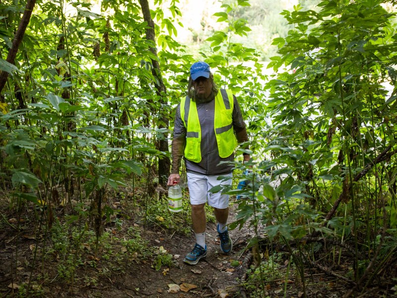 Tom Christal walks through thick brush in a mosquito resistant outfit to deliver food and water for cats. Photo by Scott Ball.