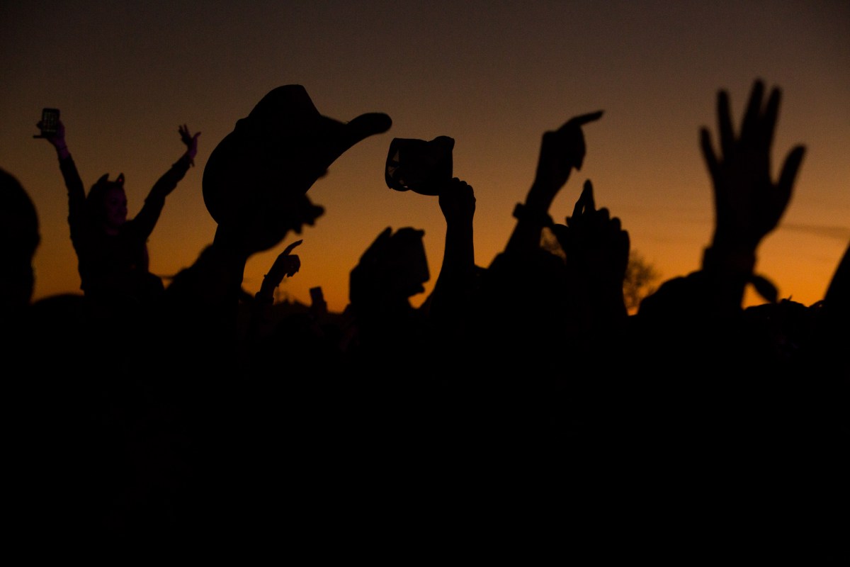 Attendees raise their hands, phones, and a cowboy hat into the air during a performance by Carnage.