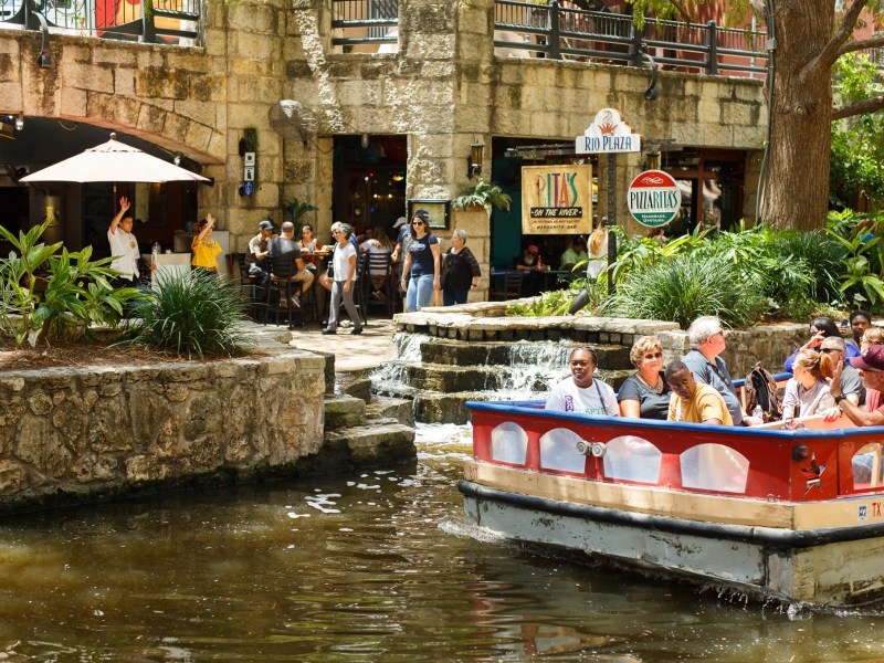 A river barge passes Rita's On the River on the San Antonio River.